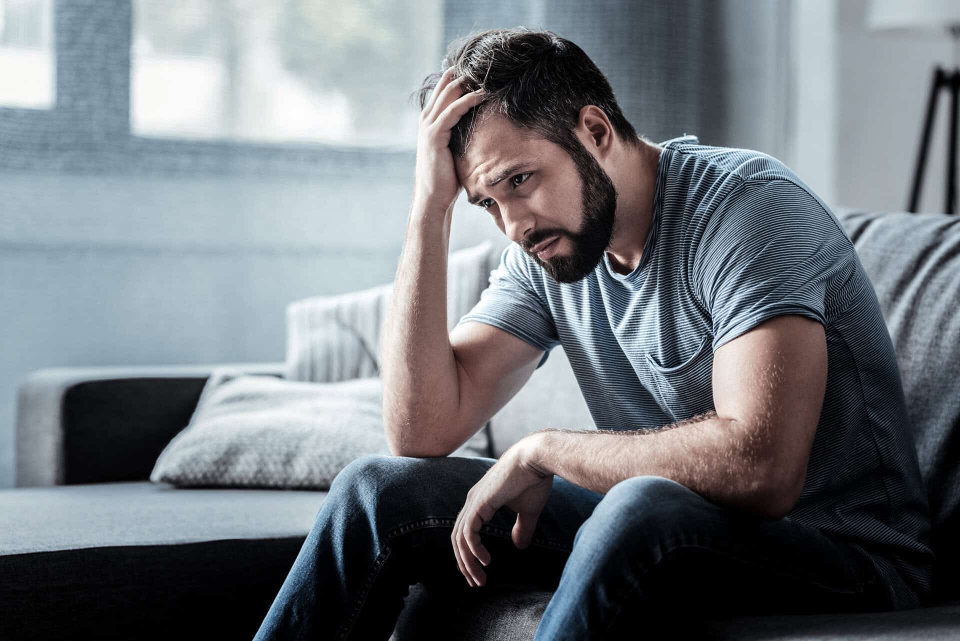 A man sitting on a couch with his head in his hand, depicting the fentanyl use damage and mental health toll of a dual diagnosis disorder.