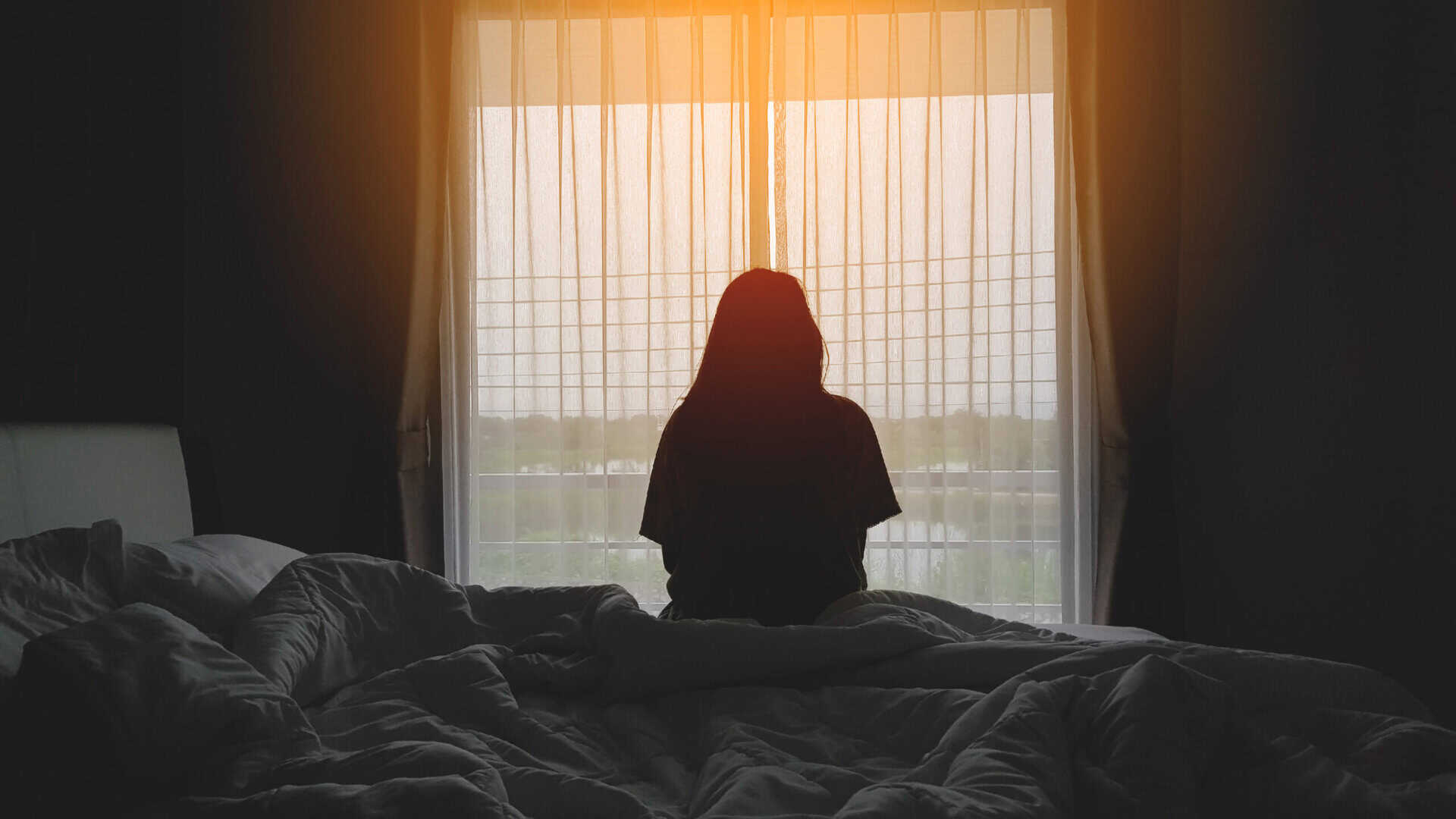 A young woman looking out a window, illustrating the persistent lethargy and social withdrawal often associated with clinical depression and major depressive disorder.