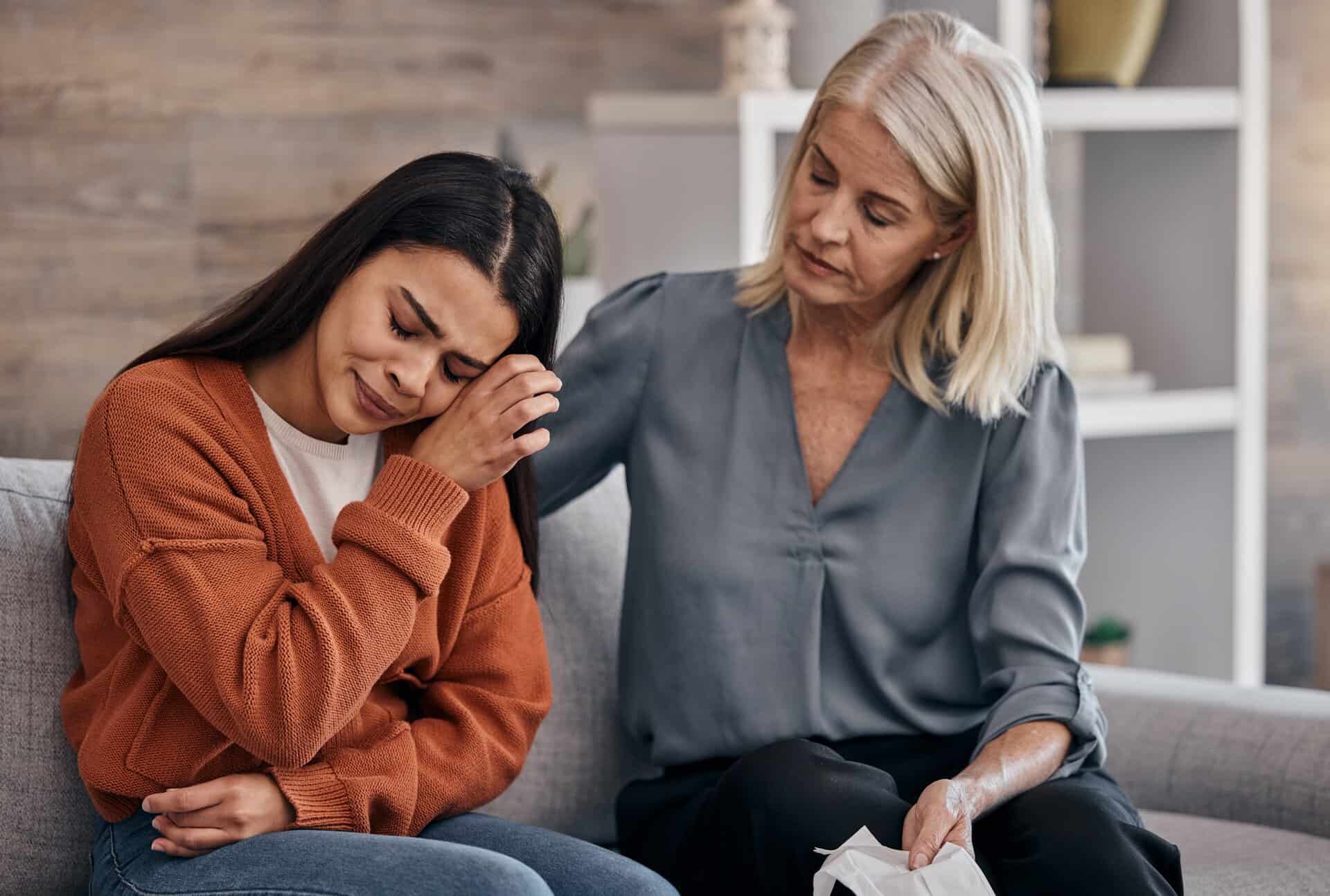 A compassionate therapist or counselor comforting a young woman who is crying during an individual counseling session on a gray sofa.