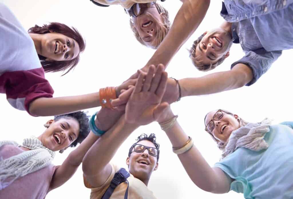 Diverse group of individuals in a recovery alumni network putting their hands together to symbolize lifelong peer support.