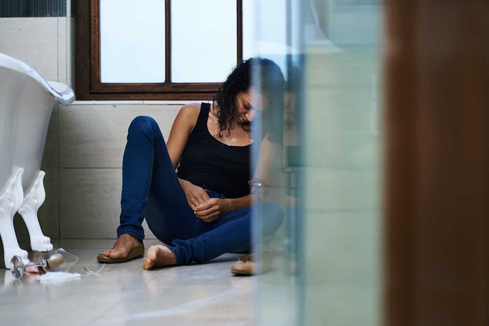 A person sitting alone on a bathroom floor looking distressed, illustrating the physical and emotional struggle often associated with the early stages of withdrawal or addiction.