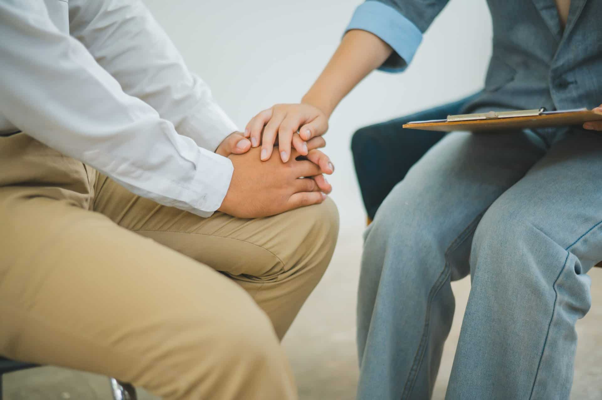 A close-up of a therapist placing a supportive hand on a patient's hand during an individual counseling session, symbolizing empathy and clinical support in mental health recovery.