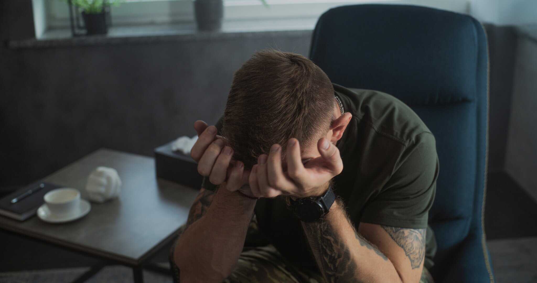 A man sitting at a desk with his head in his hands, illustrating the overwhelming emotional distress and psychological weight associated with untreated PTSD and complex trauma.