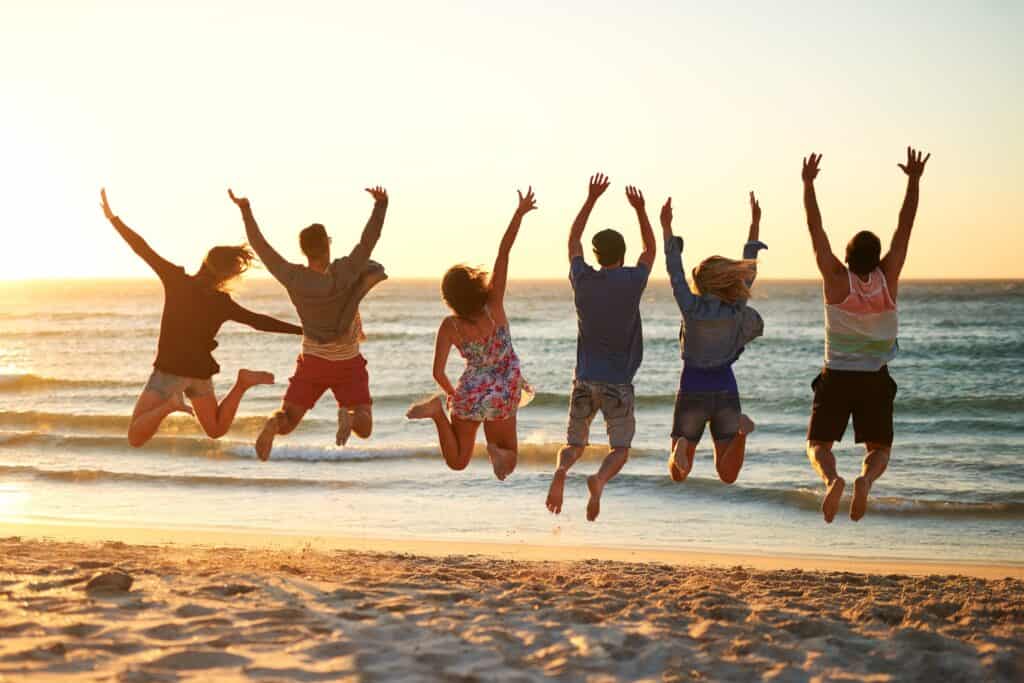 A group of alumni celebrating long-term recovery by jumping on the beach at sunset during a community event.