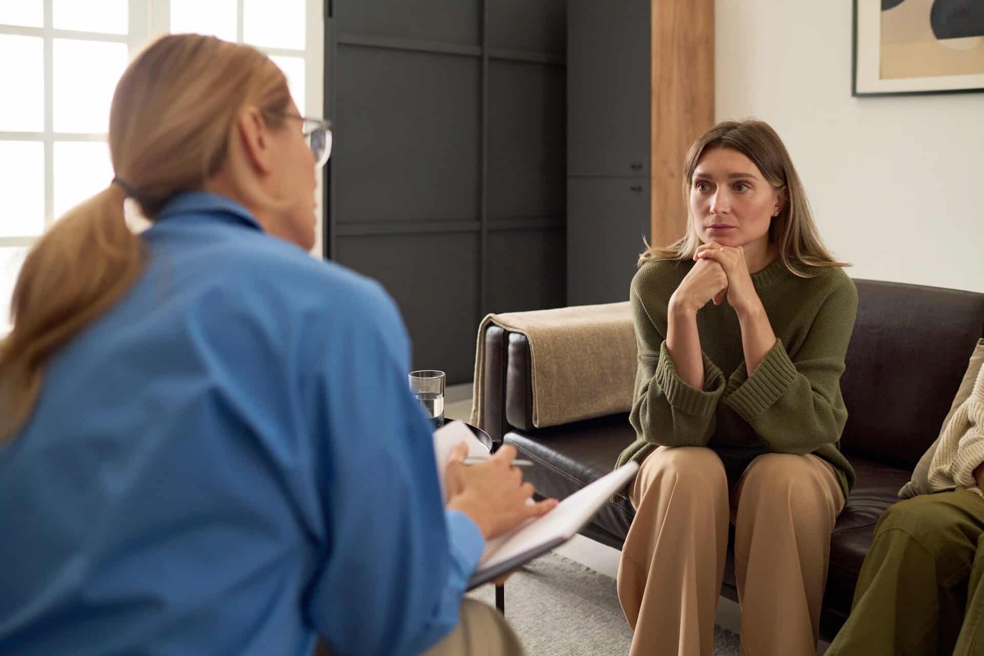 A woman sitting on a couch during a therapy session talking to a female doctor.