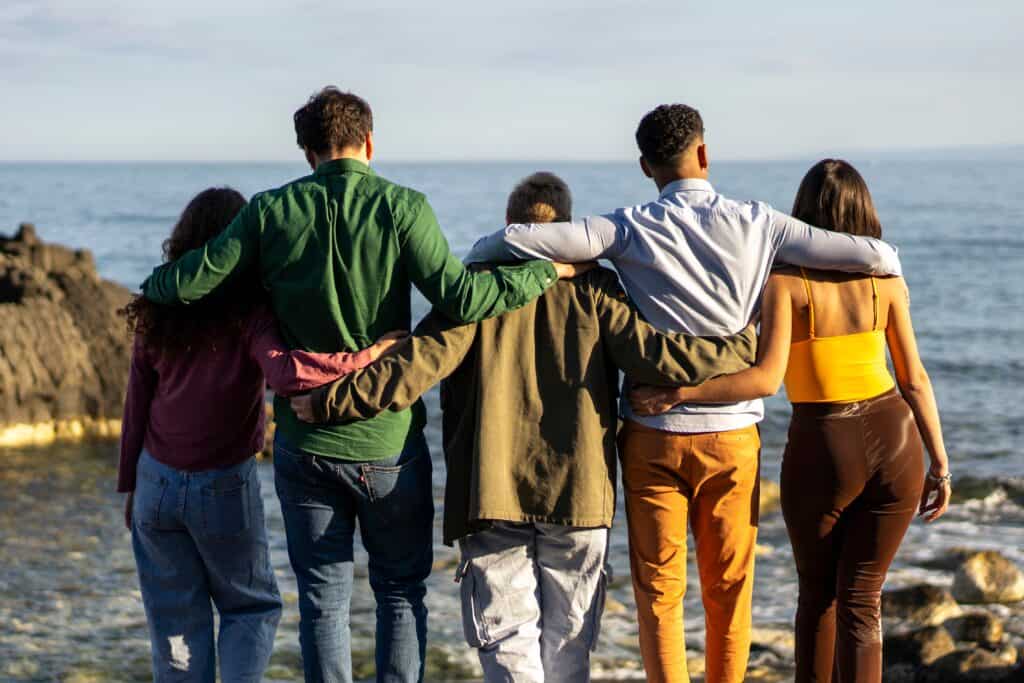 A group of people with their arms around each other looking out at the ocean, representing the peer support, community, and long-term wellness found in a continuum of care network.